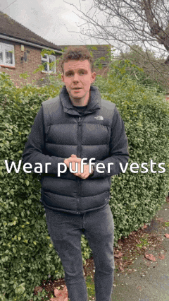a man wearing a north face vest stands in front of a bush