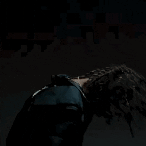 a man with dreadlocks is wearing a black jacket and a black shirt and giving the middle finger .