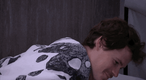 a man is laying on a bed wearing a white shirt with a black and white pattern .