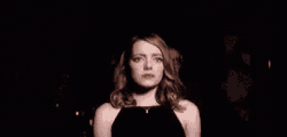 a woman in a black dress is standing in a dark room looking at the camera .