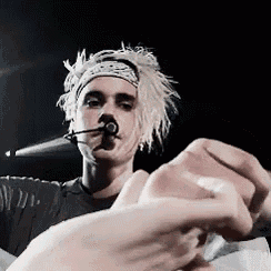 a man wearing a headband is singing into a microphone while a woman holds his hand .
