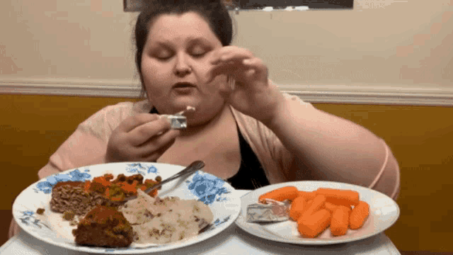 a woman eating a plate of food next to a plate of carrots on a table