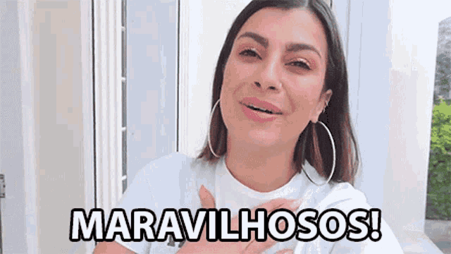 a woman wearing hoop earrings and a white t-shirt says maravilhosos !