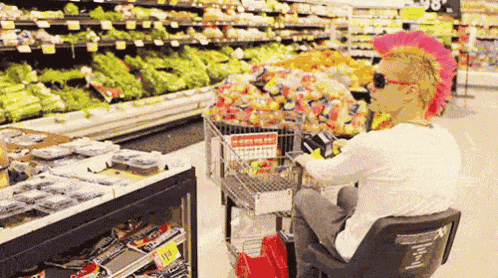 a man wearing a pink mohawk is sitting in a chair in a grocery store
