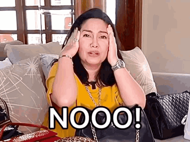 a woman is sitting on a couch with her hands on her head and the words nooo written on her face .