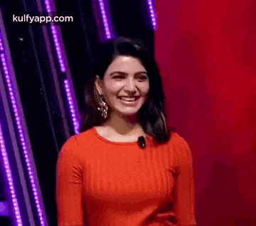 a woman in a red sweater is smiling in front of a purple background .