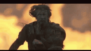 a man is running in front of a fire with a gun in his hand .