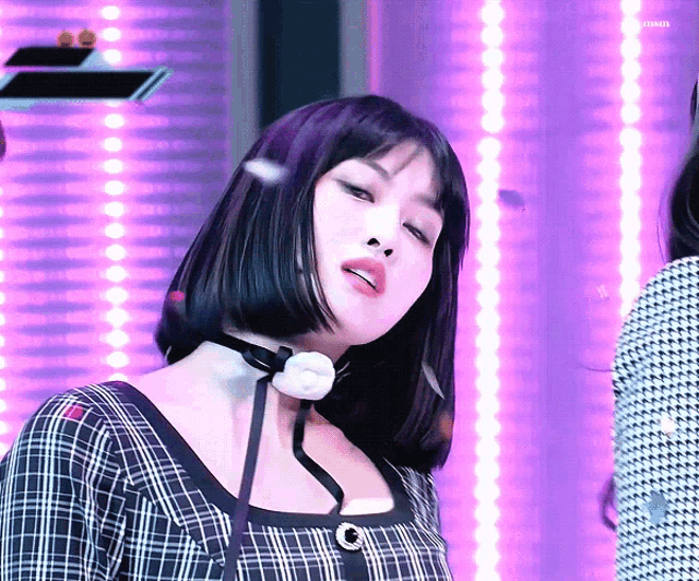 a woman wearing a choker and a plaid dress is standing in front of purple lights