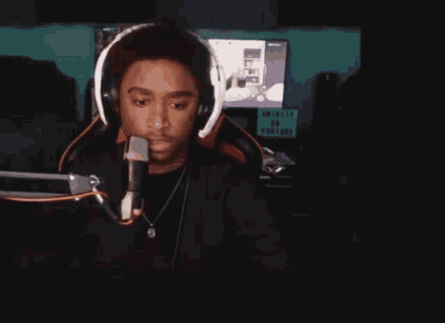 a man wearing headphones stands in front of a microphone with a sign behind him that says " ariel "