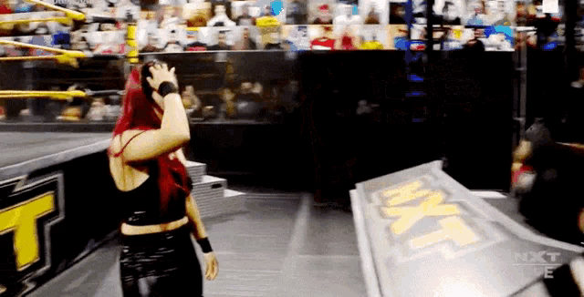 a woman with red hair is standing in front of a sign that says nxt live
