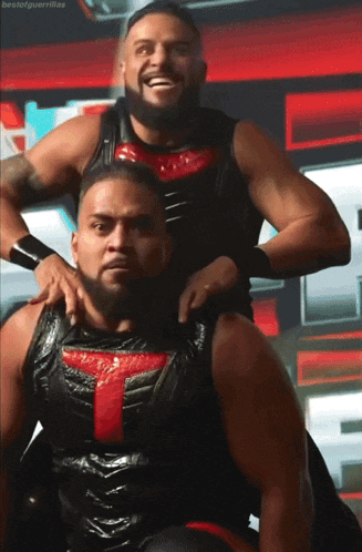 two wrestlers are posing for a picture and one of them has a red t on his chest