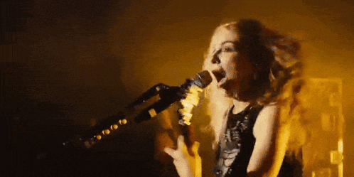 a woman is singing into a microphone in a dark room