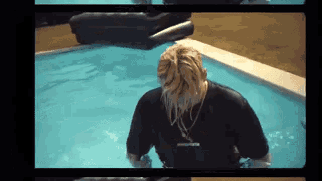 a man is standing in a swimming pool wearing a black shirt and a necklace .