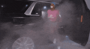a woman in a pink shirt that says diamond is standing next to a car