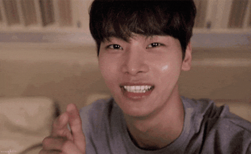 a young man is smiling and pointing at the camera while wearing a grey shirt .