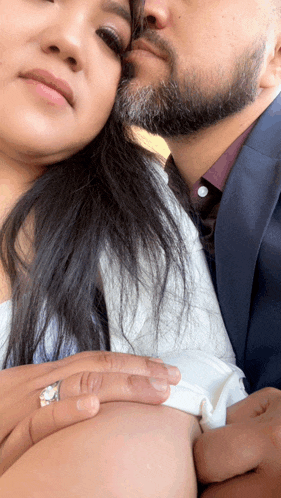 a man with a beard kisses a woman on the forehead who is wearing an engagement ring