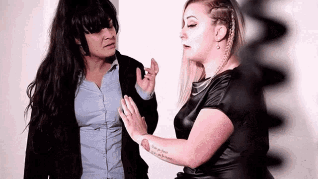 two women are standing next to each other and talking . one of the women has a tattoo on her arm .