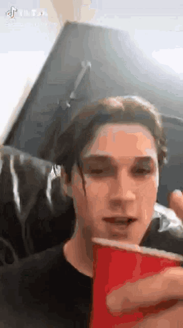 a young man is holding a red cup in his hand while looking at his phone .