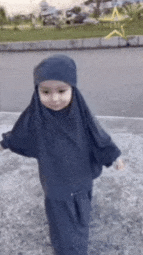 a little girl wearing a hijab and a hat is walking down the street
