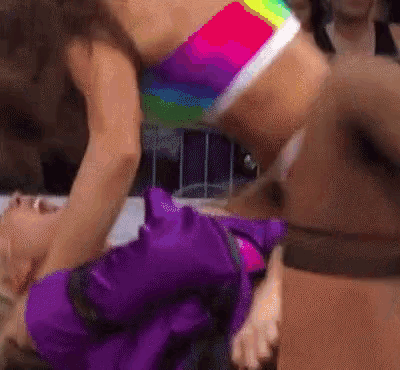 a woman in a purple dress is being pinned down by another woman in a rainbow top .