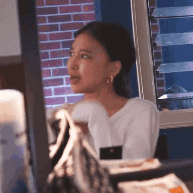 a woman in a white shirt is looking out a window