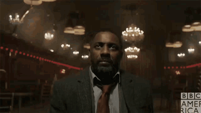 a man in a suit and tie is in a dark room with bbc america written on the bottom right