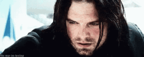 a close up of a man with long black hair and a beard looking down .