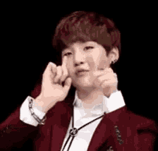 a young man in a red jacket and white shirt is making a heart shape with his hands .