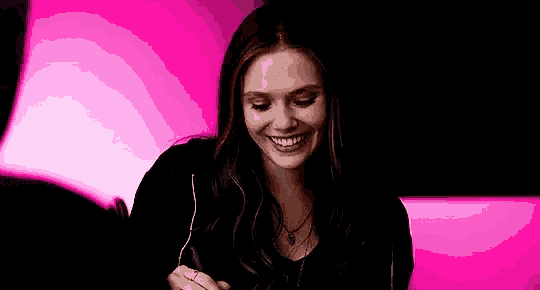 scarlet witch is smiling while holding a pen in front of a pink background .