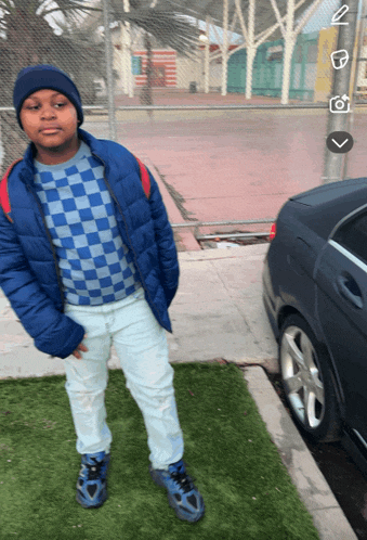 a boy wearing a blue jacket and white pants is standing next to a car