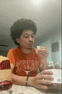 a man wearing a red texas shirt is eating a sandwich .