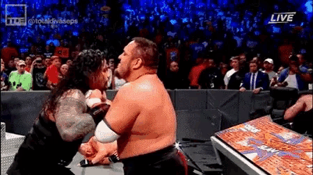 two wrestlers are fighting in a wrestling ring while a crowd watches on .