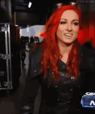 a woman with red hair is standing in front of a sign that says ' smackdown ' on it .