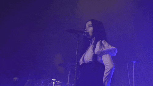 a woman singing into a microphone with a drummer in the background