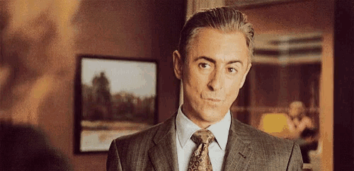 a man in a suit and tie is standing in a room looking at the camera .