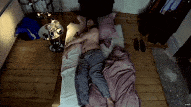 a man is laying on a bed with a purple comforter and a clock on the floor