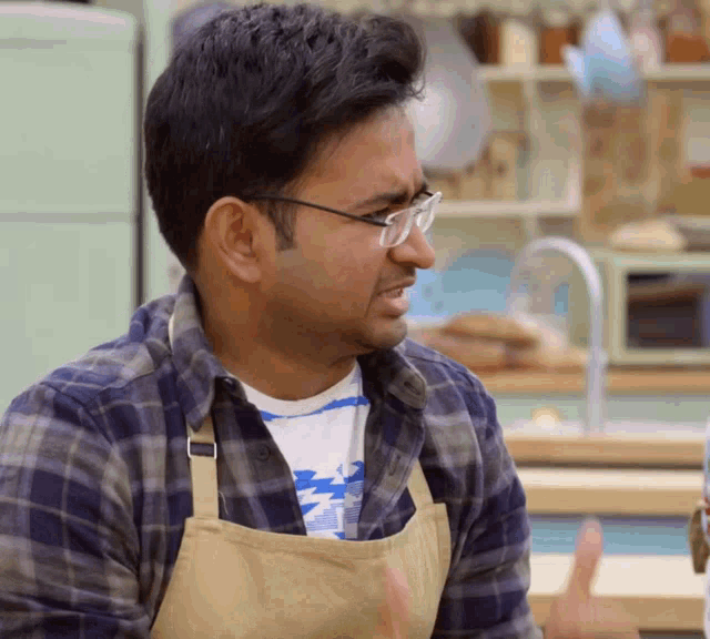 a man wearing glasses and a plaid shirt is sitting in a kitchen