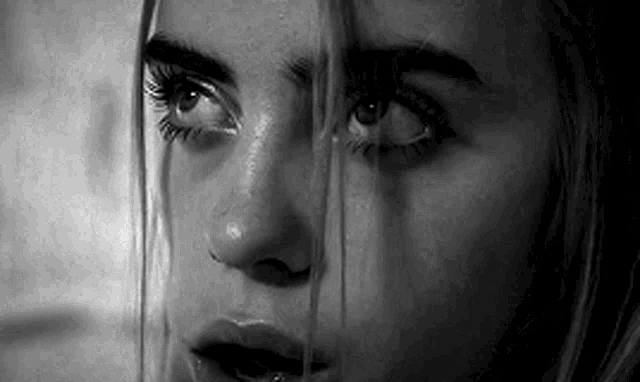 a black and white photo of a woman 's face with a tear running down her cheek .