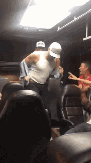 a man in a white tank top and a hat that says ' a ' on it is dancing on a bus