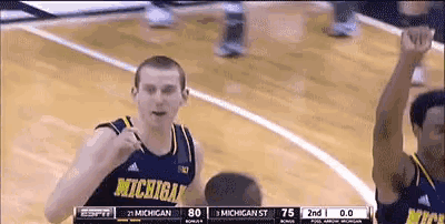 a man wearing a michigan jersey holds his fist up in the air