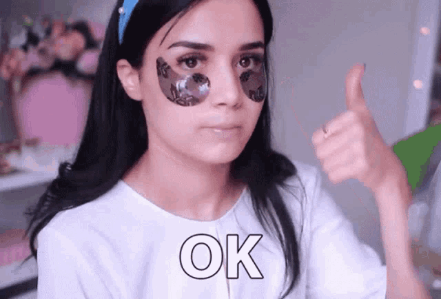 a woman with eye patches on her face is giving a thumbs up sign
