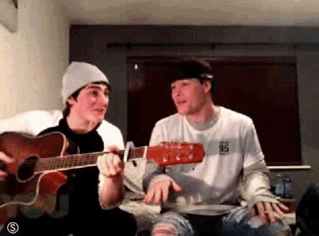 two young men are playing guitars together in a room .