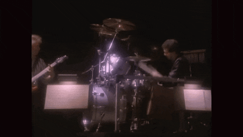 a man playing a guitar and another man playing drums on stage