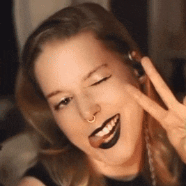a woman with black lipstick and a nose ring is smiling and giving a peace sign