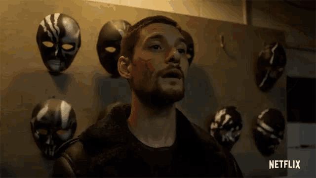 a man stands in front of a wall of masks with netflix written on the bottom right