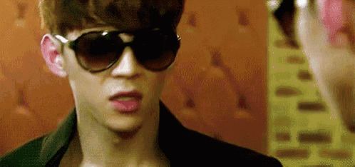 a young man wearing sunglasses and a black jacket is looking at another person .