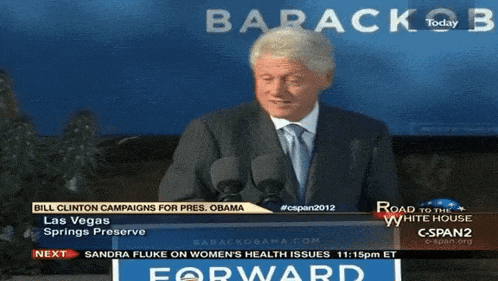 a man in a suit and tie is giving a speech in front of a screen that says barack obama