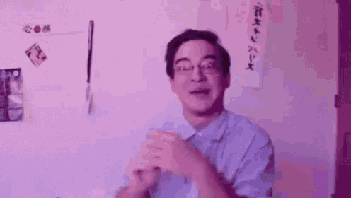 a man wearing glasses is clapping his hands in front of a wall that says oooooooh .