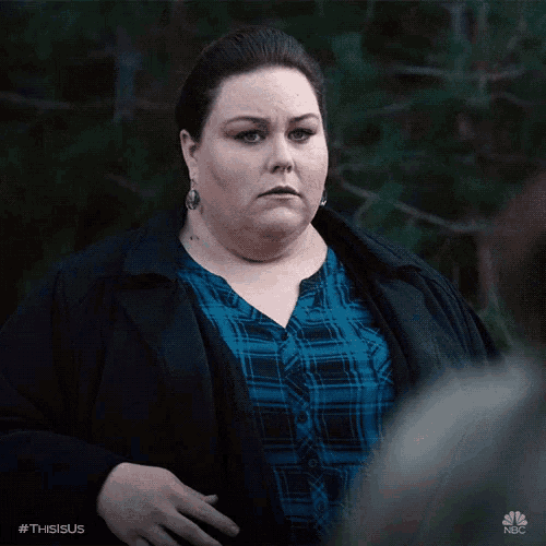 a woman in a plaid shirt and a black jacket is standing in front of trees and the hashtag #thisisus