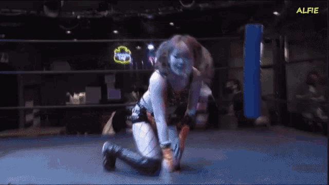 a female wrestler is kneeling down in a ring with the word alfie on the bottom